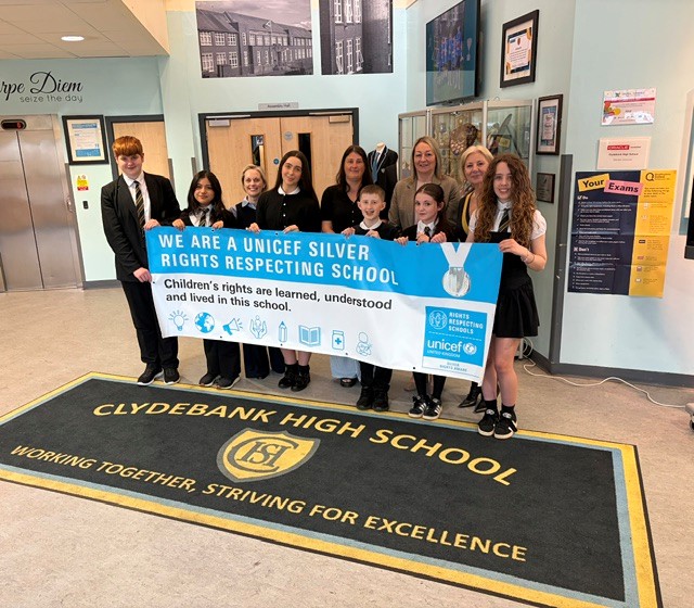 A group of Clydebank High School pupils and staff proudly holding their UNICEF Silver Rights Respecting School Award certificate outside the school building.