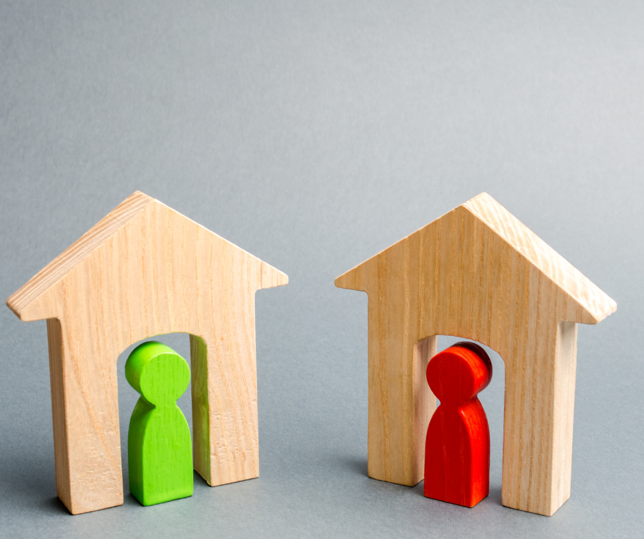 Two wooden houses with one green figure and one red figure in the doors