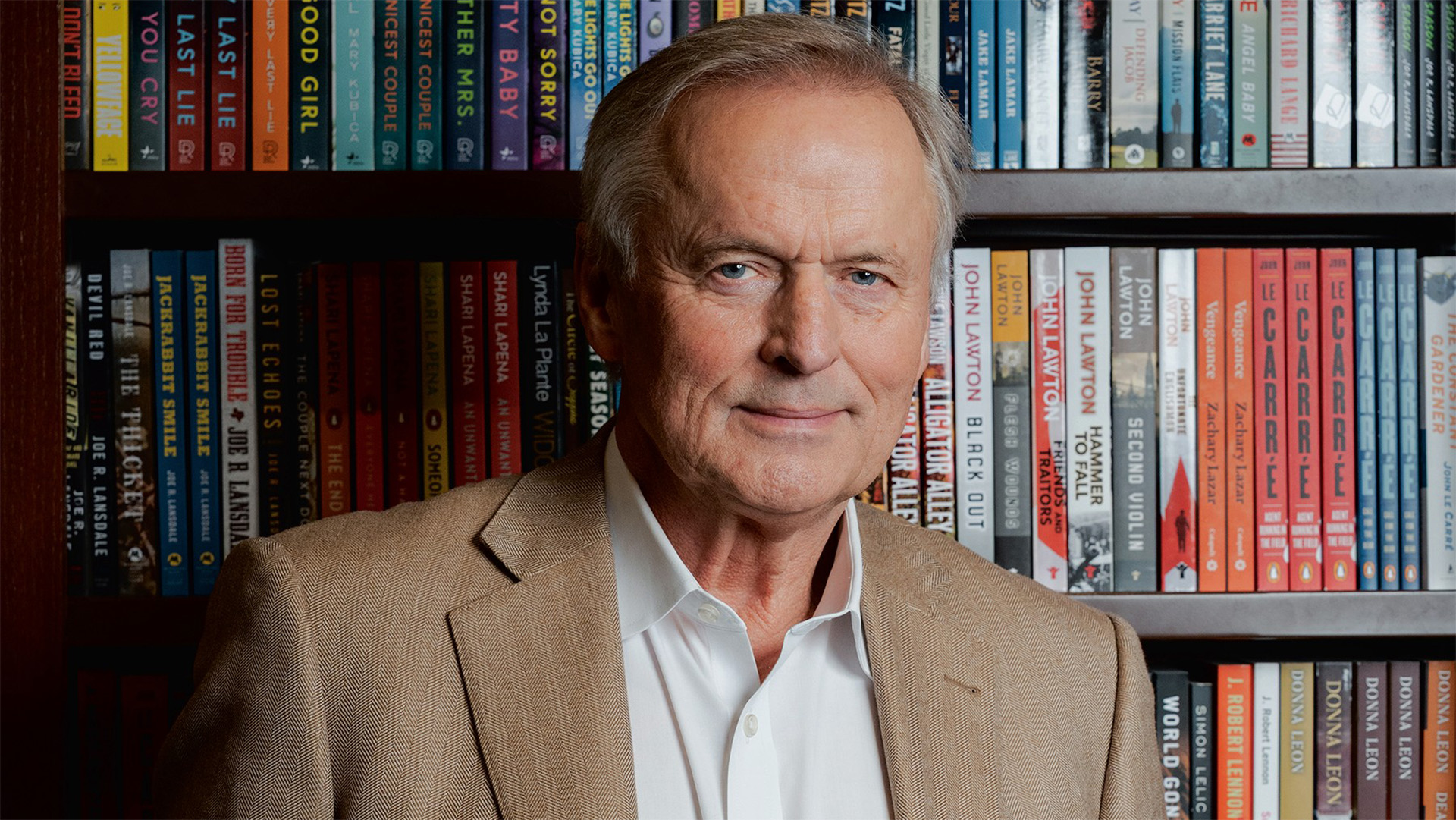 John Grisham standing in front of a bookcase